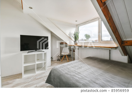 Minimalist interior design of small bedroom with soft bed placed in corner and wooden wardrobe and shelves with lamp illumination 85956959