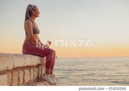 Asian woman sitting on the edge of seashore looking at sunset Asian woman sitting on the edge of seashore looking at sunset 85958266