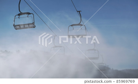4k empty ski lifts against blue sky in motion, artificial snow sprayed by snow cannon in sunny winter, bottom view. Artificial snow cloud, backdrop of working chair lift without people in ski resort 4k empty ski lifts against blue sky in motion, artificial snow sprayed by snow cannon in sunny winter, bottom view. Artificial snow cloud, backdrop of working chair lift without people in ski resort 85969769