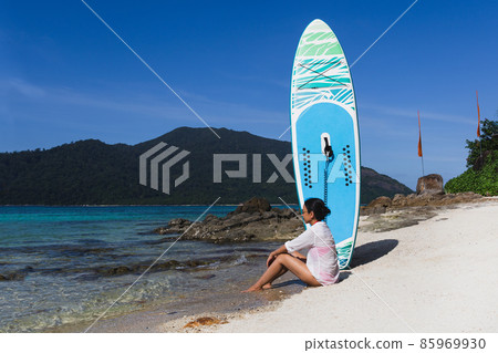 Female surfer with tanned skin sitting on beach with paddle board. Female surfer with tanned skin sitting on beach with paddle board. 85969930