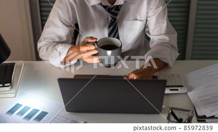 Overwork Concept An office man who works late drinking a cup of coffee while concentrating on his work on the notebook Overwork Concept An office man who works late drinking a cup of coffee while concentrating on his work on the notebook 85972839