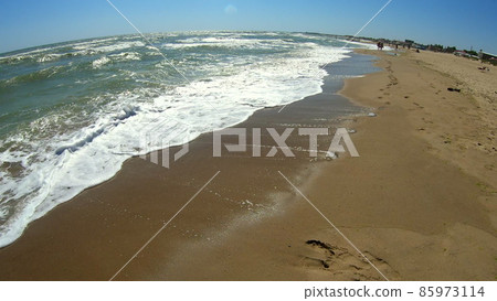 Sea wave with white foam rolls over sandy shore of beach. Top view. Sea wave with white foam rolls over sandy shore of beach. Top view. 85973114
