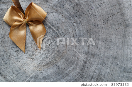 Shiny golden bow on the rough surface of an old stump with a cleft 85973383