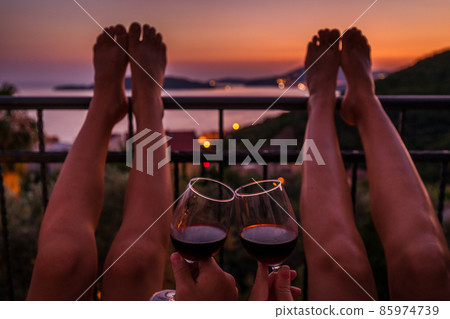 Valentine day concept image of legs of persons drink wine at the sea view balcony at sunset Valentine day concept image of legs of persons drink wine at the sea view balcony at sunset 85974739