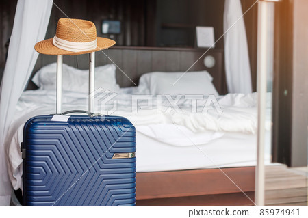 Blue Luggage with hat in modern hotel room after door opening. Time to travel, service, journey, trip, summer holiday and vacation concepts 85974941