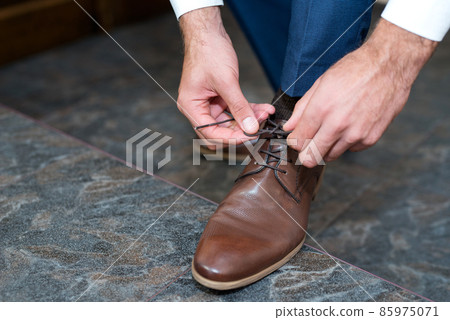 A young man ties the laces of his shoes - detail, selective fokus A young man ties the laces of his shoes - detail, selective fokus 85975071