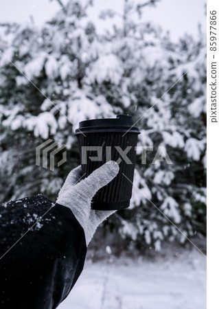 Female hand in winter warm gloves holding black eco paper cup. Winter picnic outdoors. Creative trendy zero waste recycle cup. Mockup. Hot warming drink to go in winter day. Take away concept Female hand in winter warm gloves holding black eco paper cup. Winter picnic outdoors. Creative trendy zero waste recycle cup. Mockup. Hot warming drink to go in winter day. Take away concept 85977866