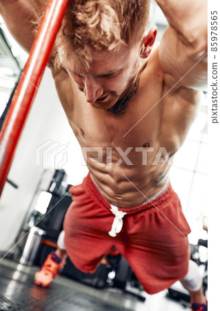 Strength concept. Male athlete using hammer during fitness workout. Fitness man beating rubber tire in gym. Muscular sportsman performing intensity training with sledgehammer in sport club 85978565