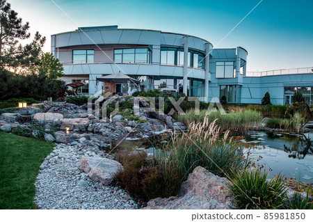 Evening summer view of modern two-story mansion with decorative pond in backyard Evening summer view of modern two-story mansion with decorative pond in backyard 85981850