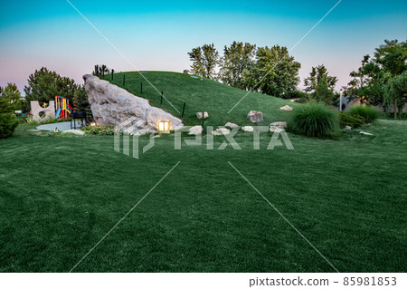 Evening view of park with green lawn, hill and playground 85981853