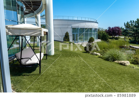 Garden swing bench with canopy near mansion on background of well-kept landscaped garden in summer 85981889