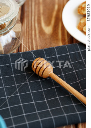 Wooden honey dipper on kitchen table with kitchenware Wooden honey dipper on kitchen table with kitchenware 85983019