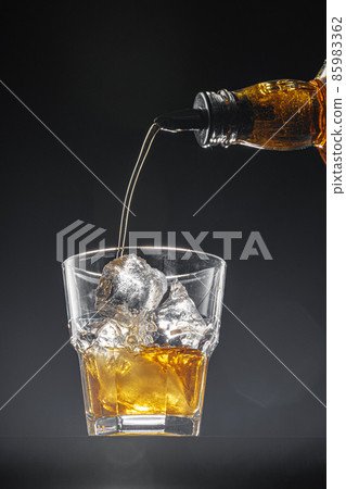 Whisky pouring into a glass on black background 85983362