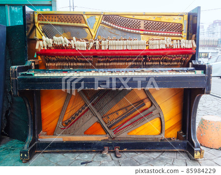 An old broken piano is on the street. Front view 85984229