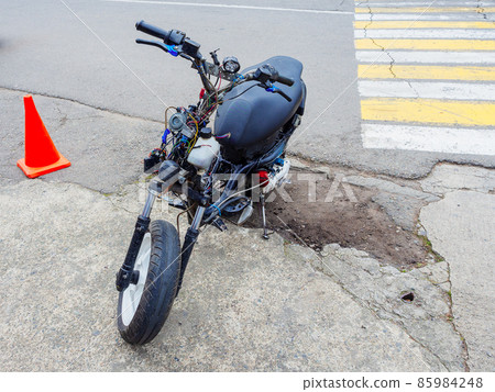 A semi-disassembled moped with wires sticking out is parked on the side of a road with broken asphalt A semi-disassembled moped with wires sticking out is parked on the side of a road with broken asphalt 85984248