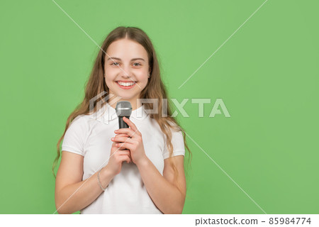 happy child singing in microphone on green background with copy space, music 85984774