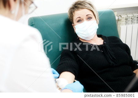 Rehabilitation and treatment in medical clinic. 40-50 year old woman in medical mask sits in chair 85985001