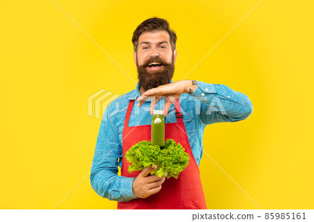 Happy man in apron holding fresh leaf lettuce holding juice bottle yellow background, juice barman Happy man in apron holding fresh leaf lettuce holding juice bottle yellow background, juice barman 85985161