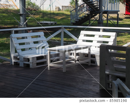 White bench and table from old wooden warehouse pallets stand on a wooden veranda in the park White bench and table from old wooden warehouse pallets stand on a wooden veranda in the park 85985198