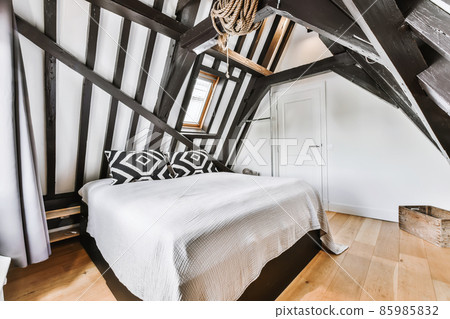 Stylish attic bedroom with wooden beams and a soft bed Stylish attic bedroom with wooden beams and a soft bed 85985832