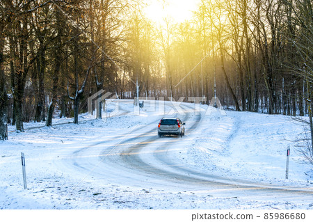 Silver car slowly driving on road along trees forest Silver car slowly driving on road along trees forest 85986680