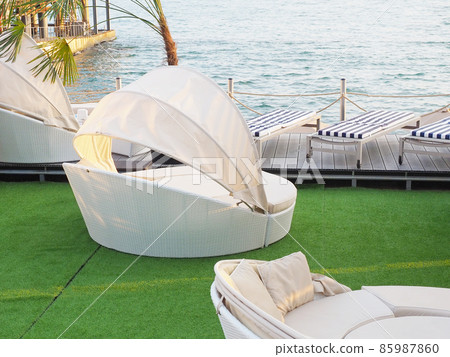 Light round rattan sofas and couches with striped mattresses in the beach recreation area against the backdrop of the sea 85987860
