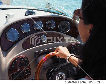 The girl controls a cruise yacht holding her hand on the steering wheel on a summer sunny day. Close-up photo The girl controls a cruise yacht holding her hand on the steering wheel on a summer sunny day. Close-up photo 85987910