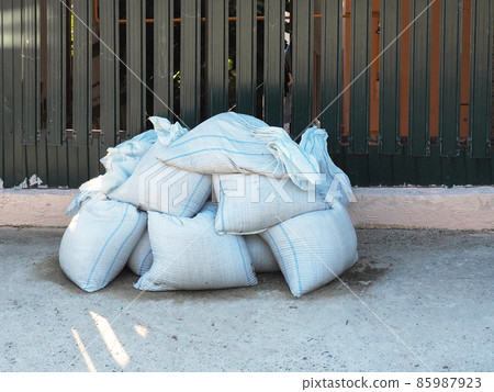 White sandbags piled up lie on the street near the fence 85987923