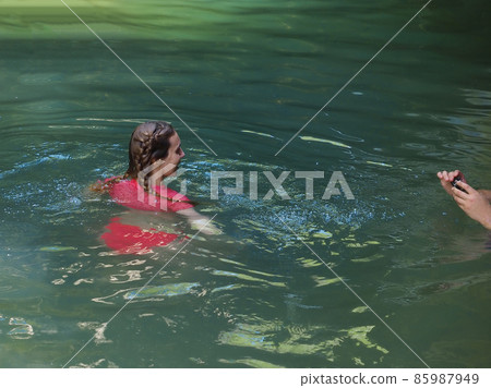 A girl poses for the camera swimming in a turquoise river of a rocky gorge 85987949