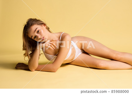 One young pretty girl, blonde in underwear lying on floor isolated over yellow studio background. Natural beauty concept. One young pretty girl, blonde in underwear lying on floor isolated over yellow studio background. Natural beauty concept. 85988000