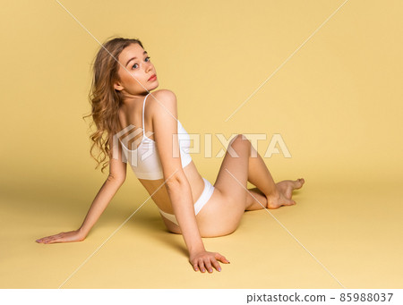 Studio shot of young adorable woman in underwear sitting on floor isolated over yellow background. Natural beauty concept. Studio shot of young adorable woman in underwear sitting on floor isolated over yellow background. Natural beauty concept. 85988037