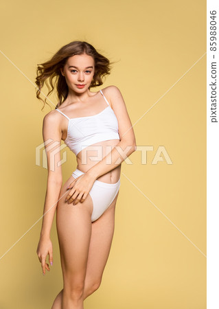 Portrait of young beautiful slim woman in underwear posing isolated over yellow studio background. Natural beauty concept. Portrait of young beautiful slim woman in underwear posing isolated over yellow studio background. Natural beauty concept. 85988046
