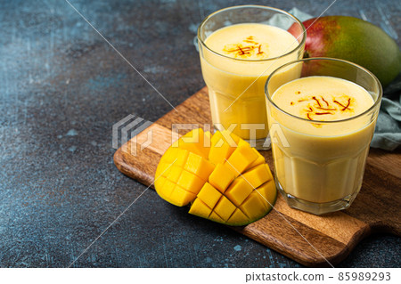 Drink mango lassi in two glasses on rustic concrete table with fresh ripe cut manfo from above Drink mango lassi in two glasses on rustic concrete table with fresh ripe cut manfo from above 85989293