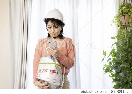 A woman wearing a helmet and carrying an emergency carry-out bag to search for an evacuation area A woman wearing a helmet and carrying an emergency carry-out bag to search for an evacuation area 85989332