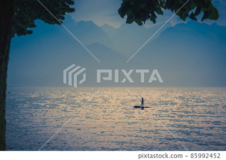 Watercolor drawing of View of mountains Alps, figure silhouette of a man on a surfboard with paddle on the Lake Leman Lake Geneva in Montreux Watercolor drawing of View of mountains Alps, figure silhouette of a man on a surfboard with paddle on the Lake Leman Lake Geneva in Montreux 85992452