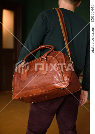 close-up photo of orange leather travel bag on mans shoulder 85993446