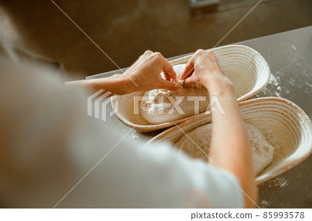 Employee makes decor on raw bread loaf in dish in light bakery 85993578