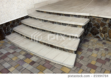 View from above of lit by sun new staircase with light tiles on background of colorful yard pavement and decorated with natural stones building wall. Professionally done work concept. 85994784