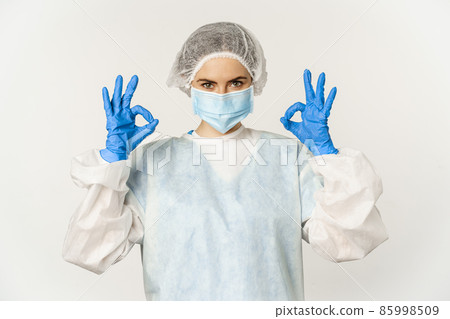 Image of healthcare worker, doctor in personal protective equipment from covid-19, showing okay ok sign, confident face in mask, standing over white background Image of healthcare worker, doctor in personal protective equipment from covid-19, showing okay ok sign, confident face in mask, standing over white background 85998509