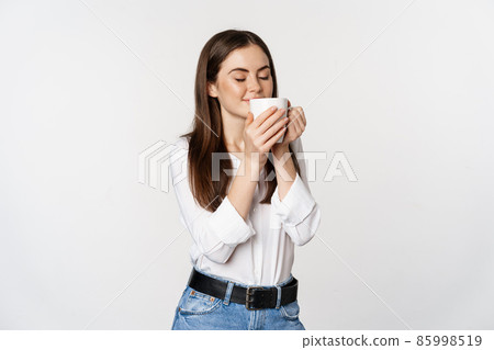 Smiling office woman drinking coffee, drink from mug with satisfaction, pleasure, standing over white background 85998519