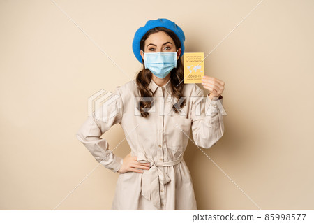Covid pandemic and travelling concept. Girl tourist in medical face mask, travel vaccinated, showing international vaccination passport during coronavirus outbreak 85998577