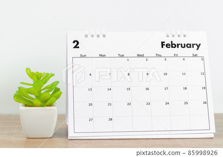 February 2022 desk calendar with plant pot on wooden table. 85998926