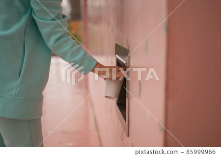 A woman throws a cup of coffee into a garbage manhole in the wall of a cafe. 85999966