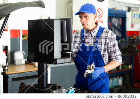 Mechanic balancing wheel with machine balancer at auto service Mechanic balancing wheel with machine balancer at auto service 86002032
