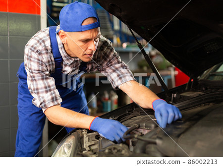 Positive man car mechanician repairing car in auto repair service Positive man car mechanician repairing car in auto repair service 86002213