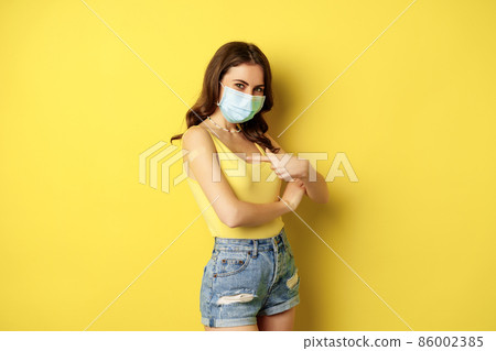 Covid-19 vaccination. Beautiful young woman in face medical mask got vaccinated during pandemic, standing over yellow background 86002385