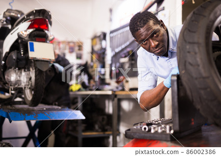 African american expert inspects the wheel of a motorcycle 86002386