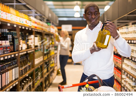 Smiling adult African man standing with bottled oil Smiling adult African man standing with bottled oil 86002494