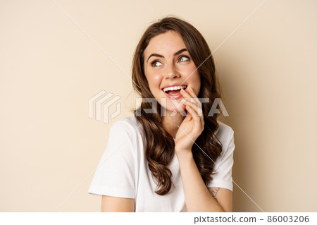 Close up portrait of coquettish beautiful girl gazing silly, gently smiling and giggling, posing flirty and cute against beige background. Women beauty and valentines concept 86003206