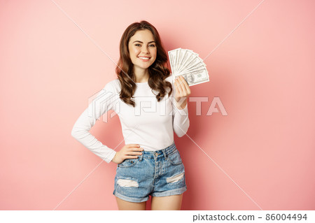 Attractive young woman holding money, cash in hands, concept of loans, microcredit and shopping, standing over pink background Attractive young woman holding money, cash in hands, concept of loans, microcredit and shopping, standing over pink background 86004494